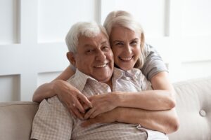 White-haired couple hugging and smiling on a couch in a well-lit room